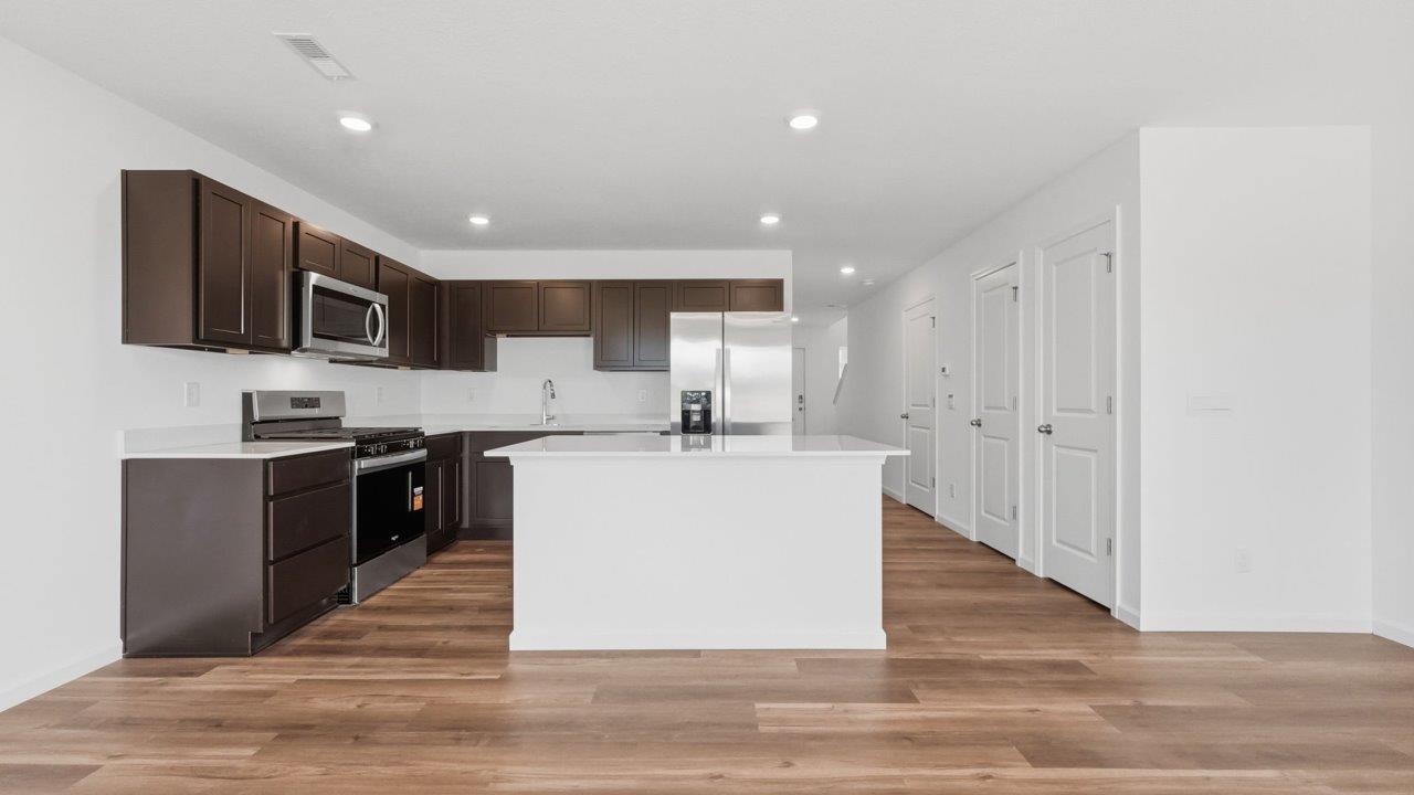 whispering pines pearson open layout kitchen with lvp flooring, sarsaparilla cabinets, stainless steel appliances, and island with bar seating