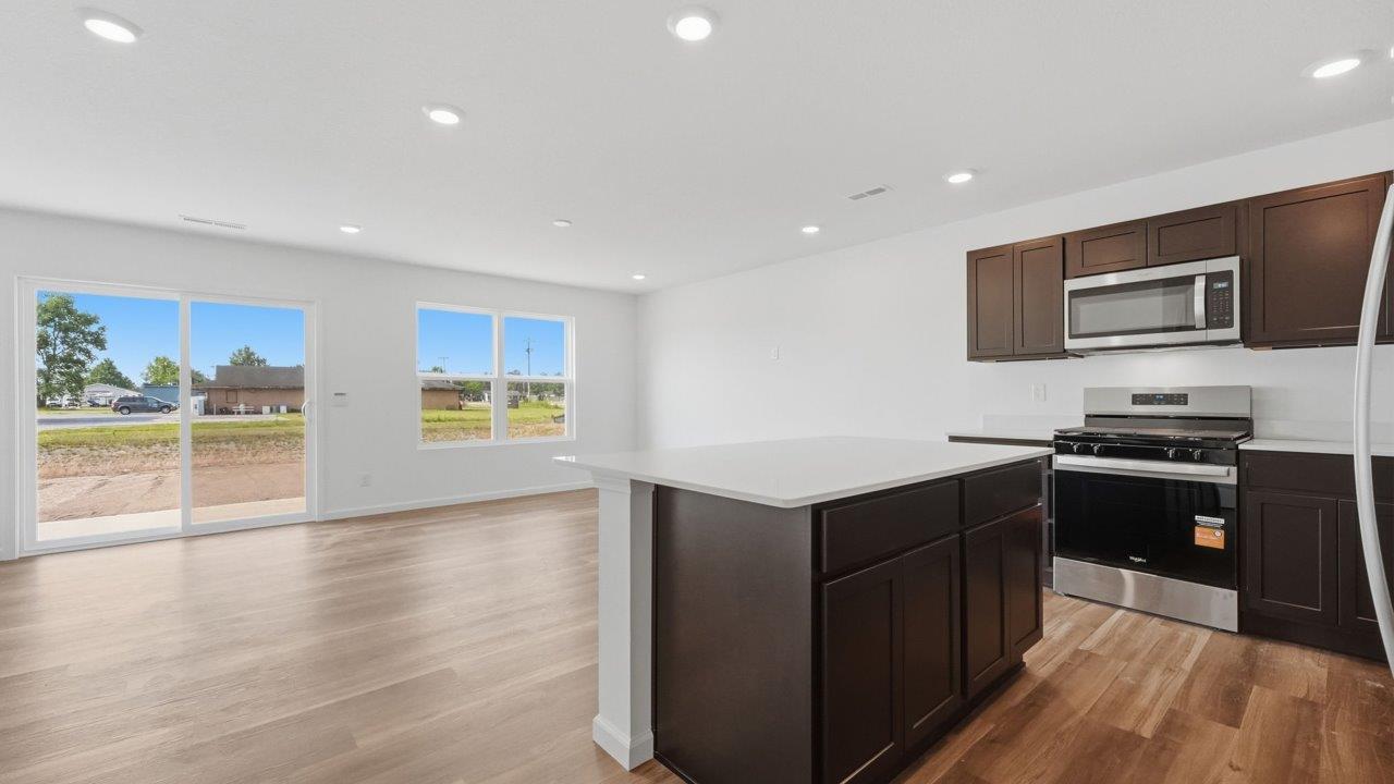 whispering pines pearson open layout kitchen with lvp flooring, sarsaparilla cabinets, stainless steel appliances, and island with bar seating