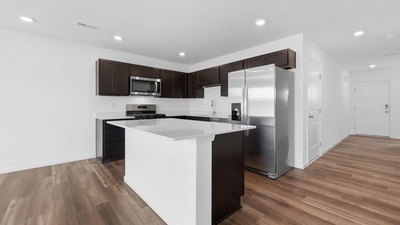 whispering pines pearson open layout kitchen with lvp flooring, sarsaparilla cabinets, stainless steel appliances, and island with bar seating