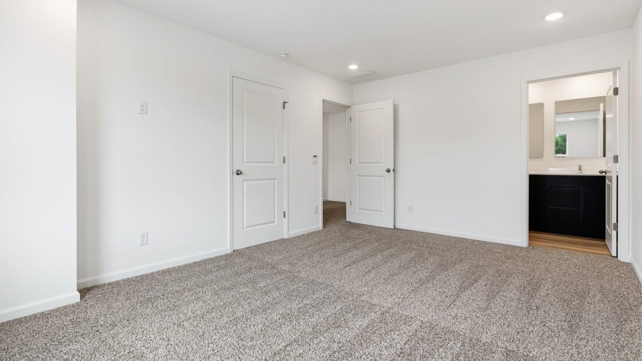 primary bedroom with carpet flooring, 2 windows, and ensuite bathroom and walk in closet
