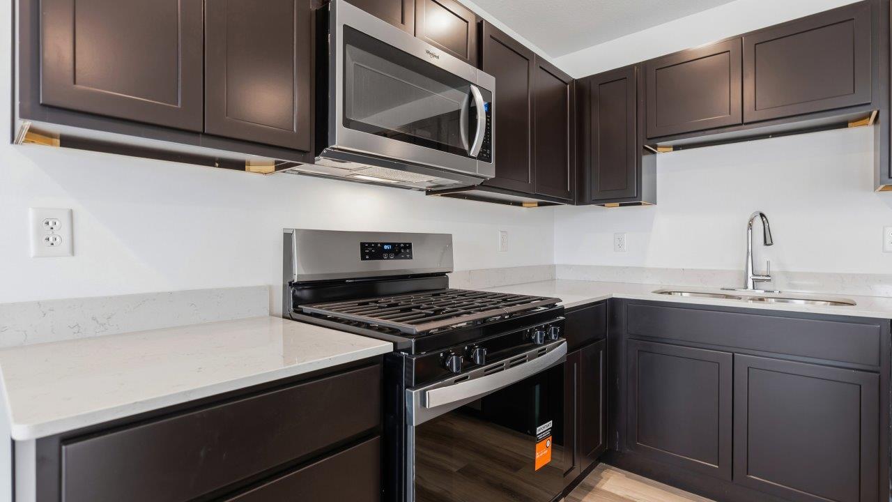 kitchen with dark brown sarsaparilla cabinets, stainless steel appliances, quartz countertops