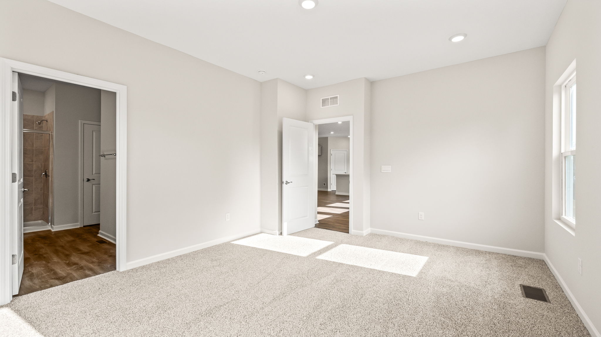 Carpeted primary bedroom with doors to bathroom and hallway