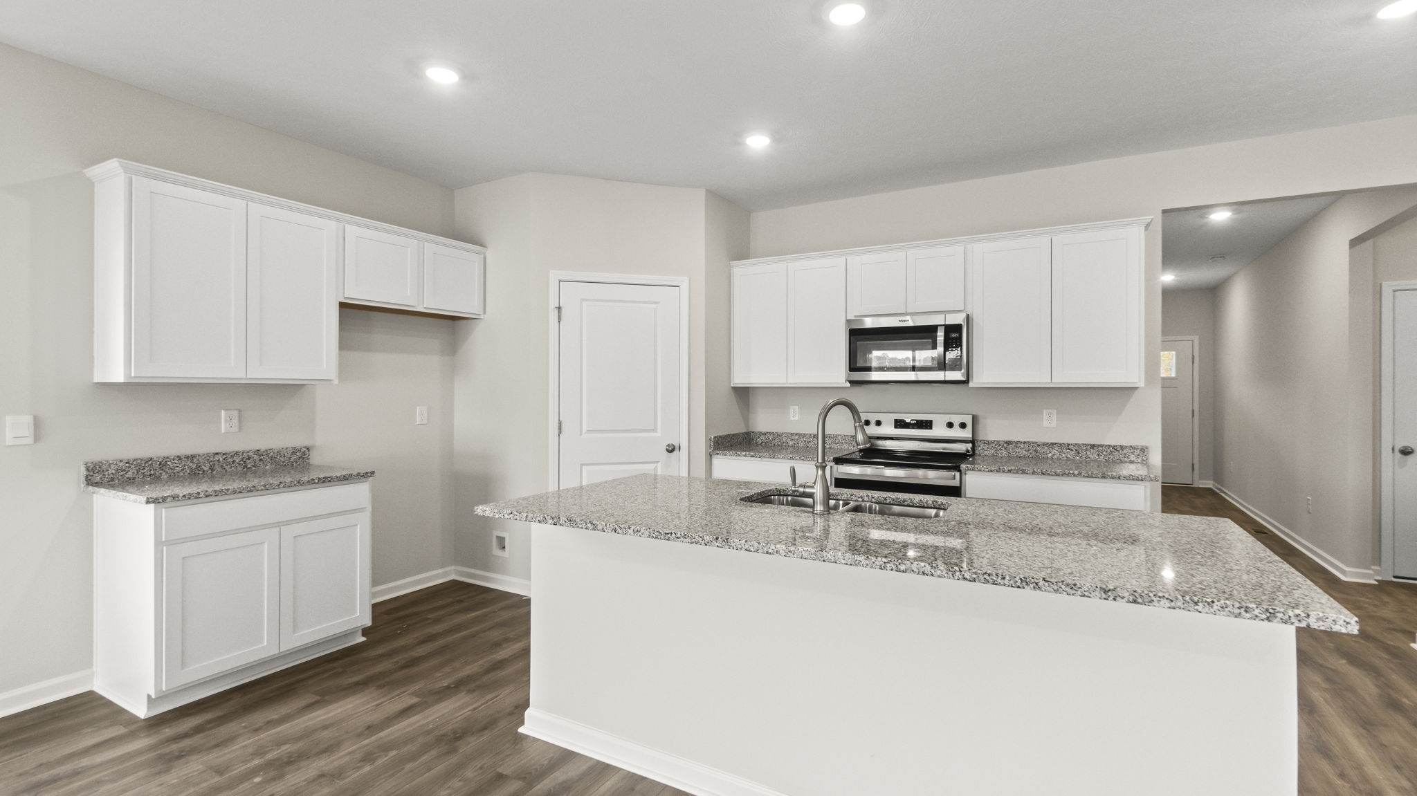 Full kitchen area with granite countertops, island, white cabinetry, and appliances