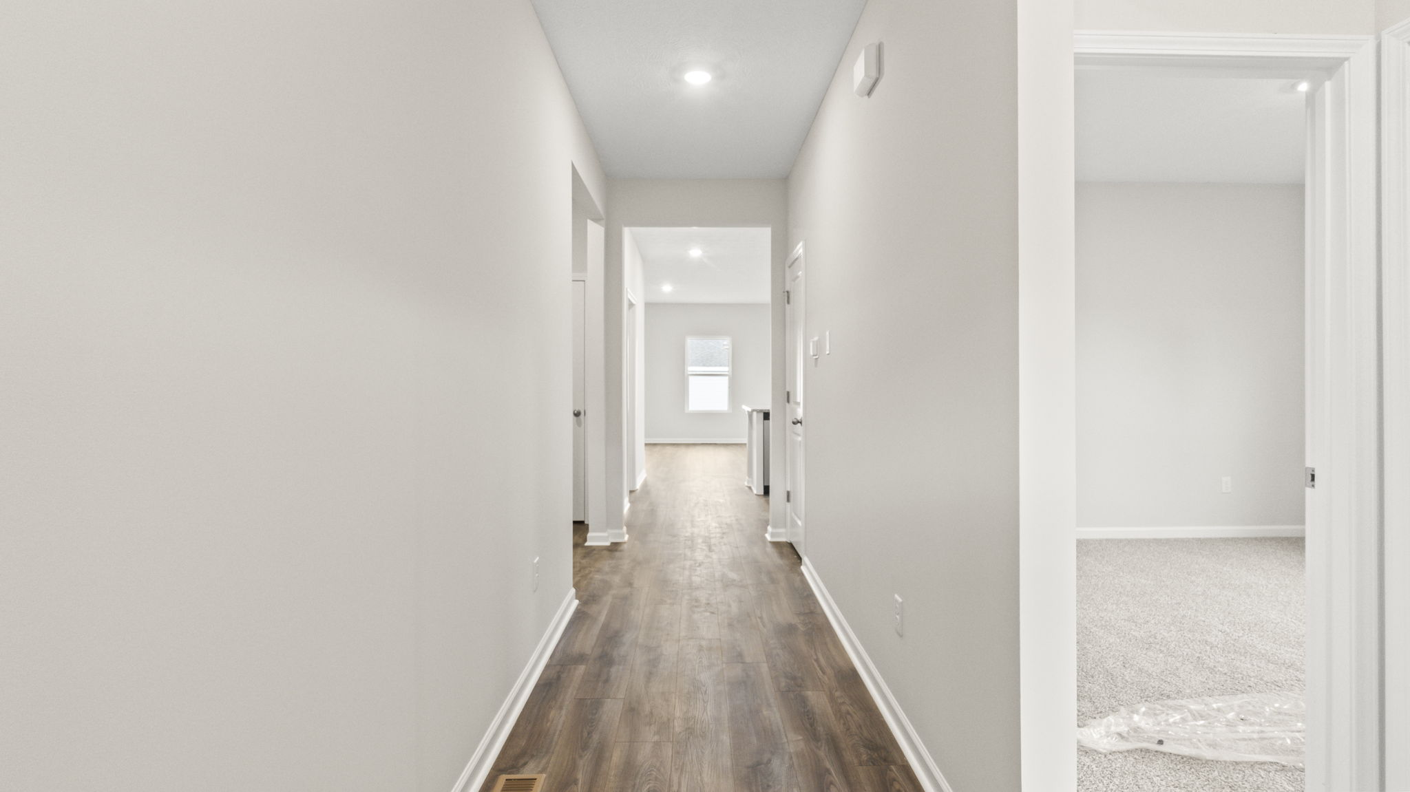 Hallway with white walls looking into a bedroom and great room