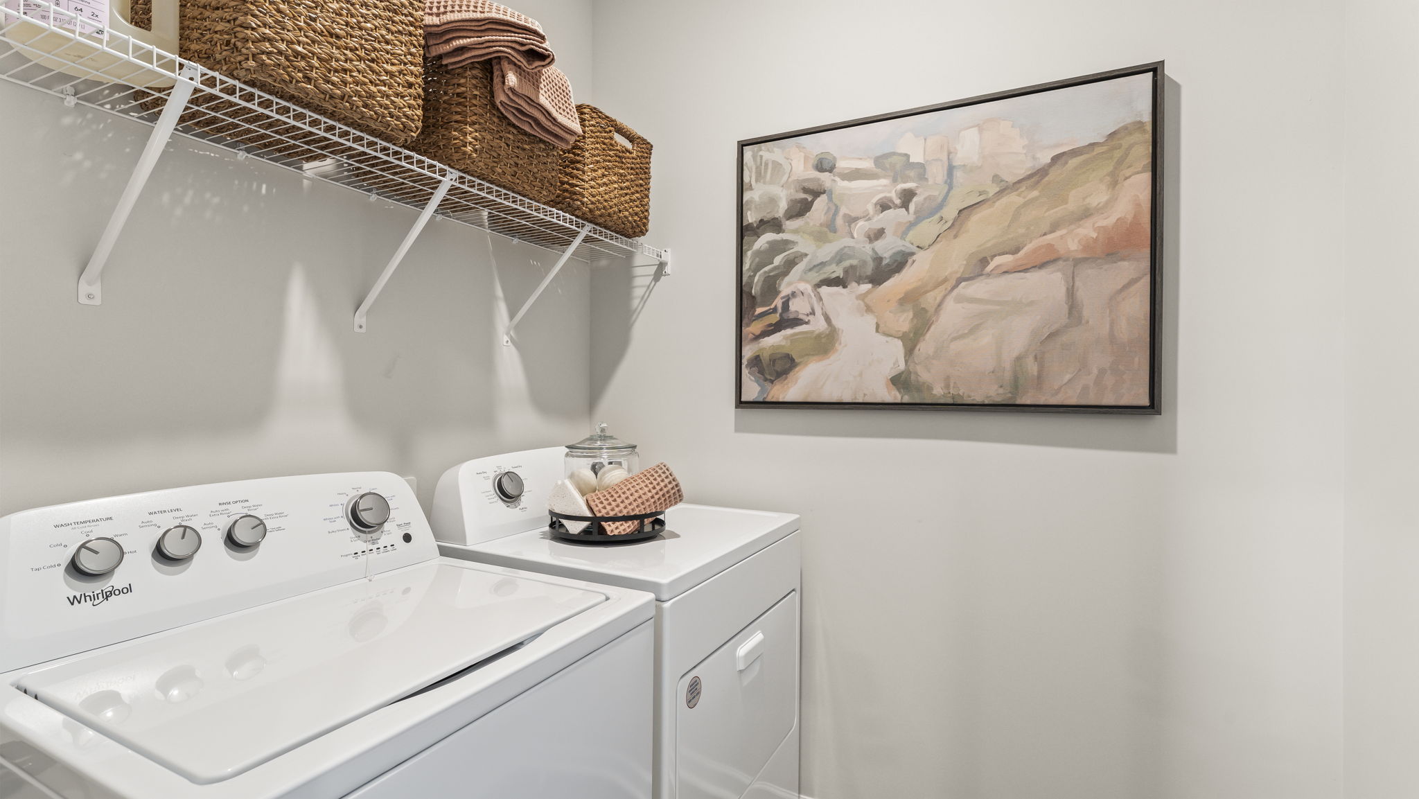 Laundry area with washer, dryer, woven baskets, wire shelving, and abstract art.