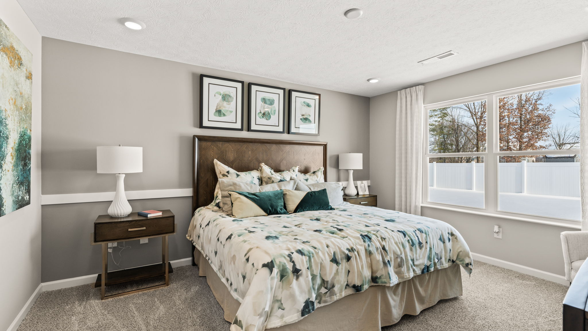 Wide angle image of the primary bedroom suite with white and green bedding and large window