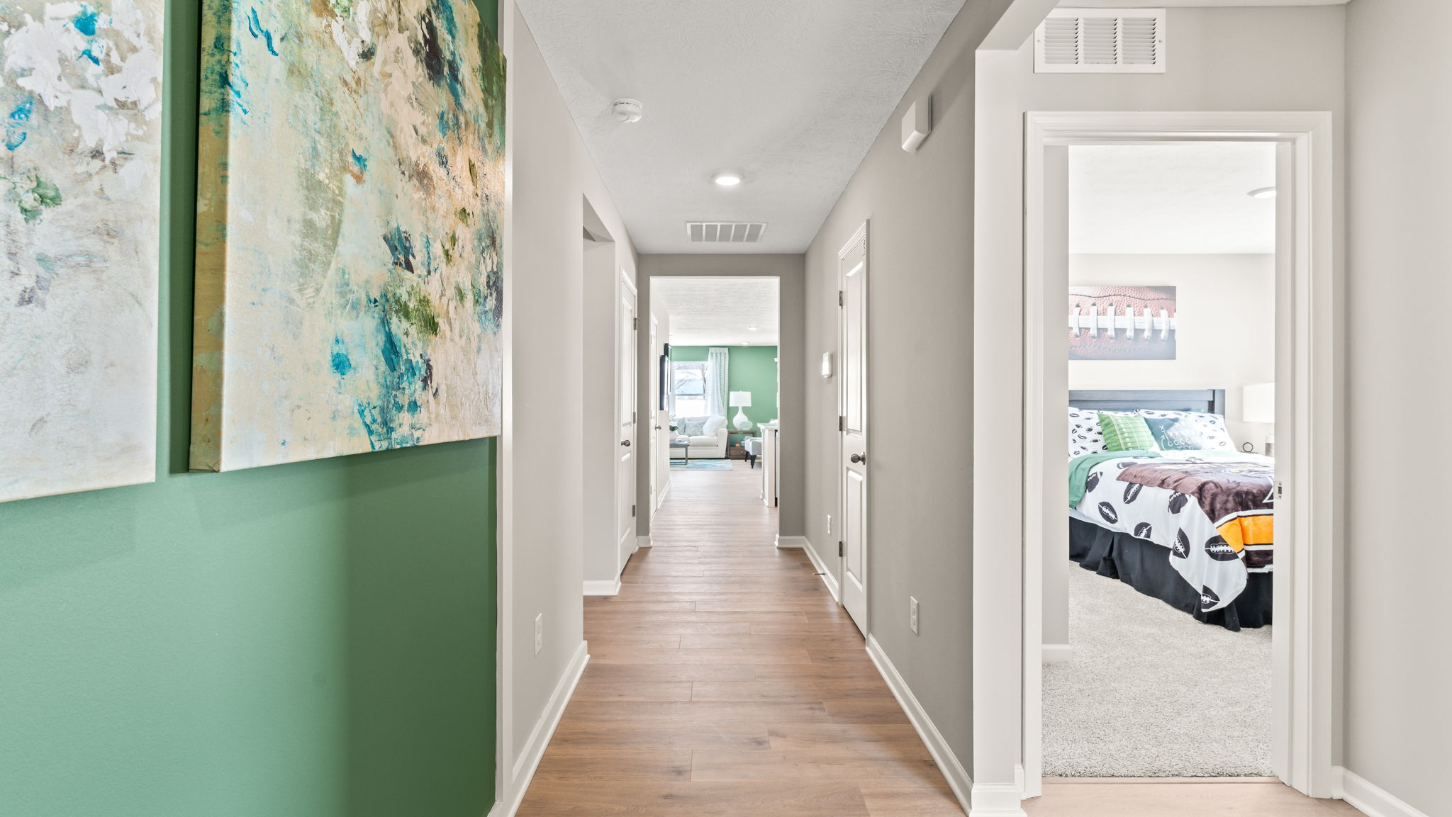 Hallway that leads into bedroom with green paint on wall and modern art decoration