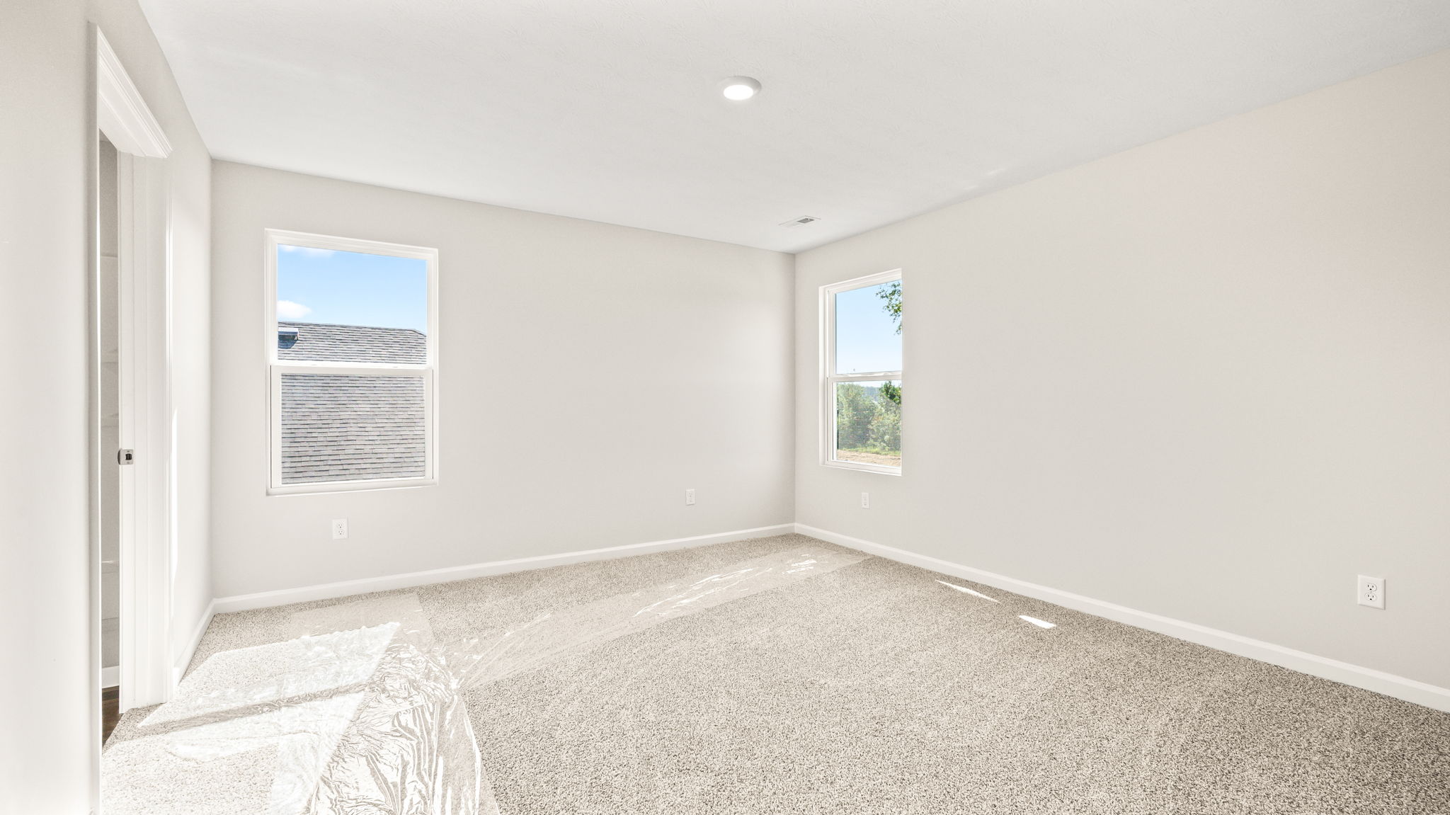 Primary bedroom with carpet, two windows, and door to primary bathroom suite visible