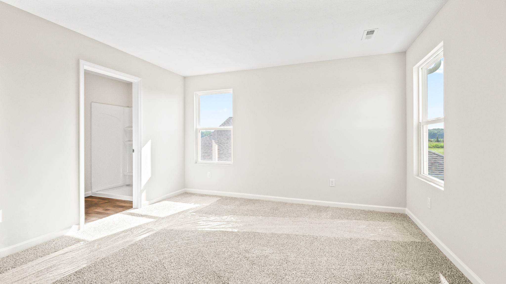 Primary bedroom with carpet, two windows, and door to primary bathroom suite visible