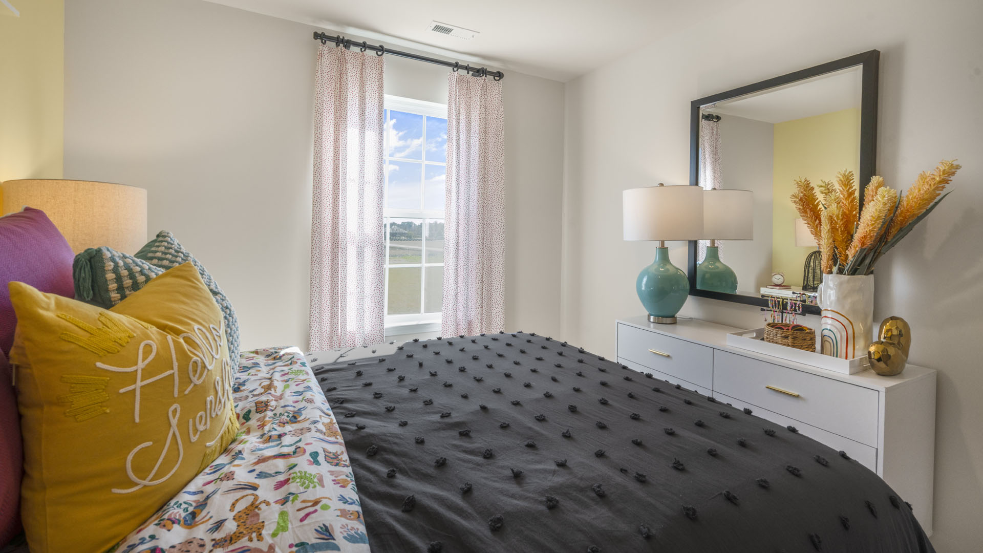 Bedroom with large lush bed and dresser with modern lamp and large mirror.