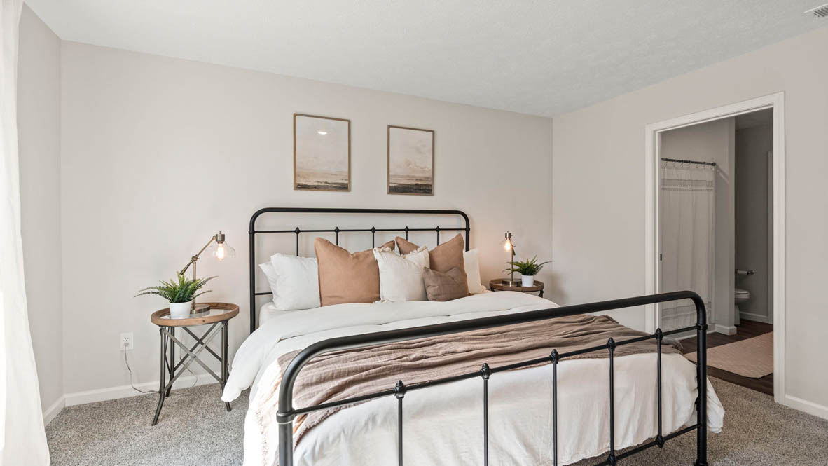 Primary Bedroom with large king size bed large windows and matching bedside tables with hallway to private bathroom.