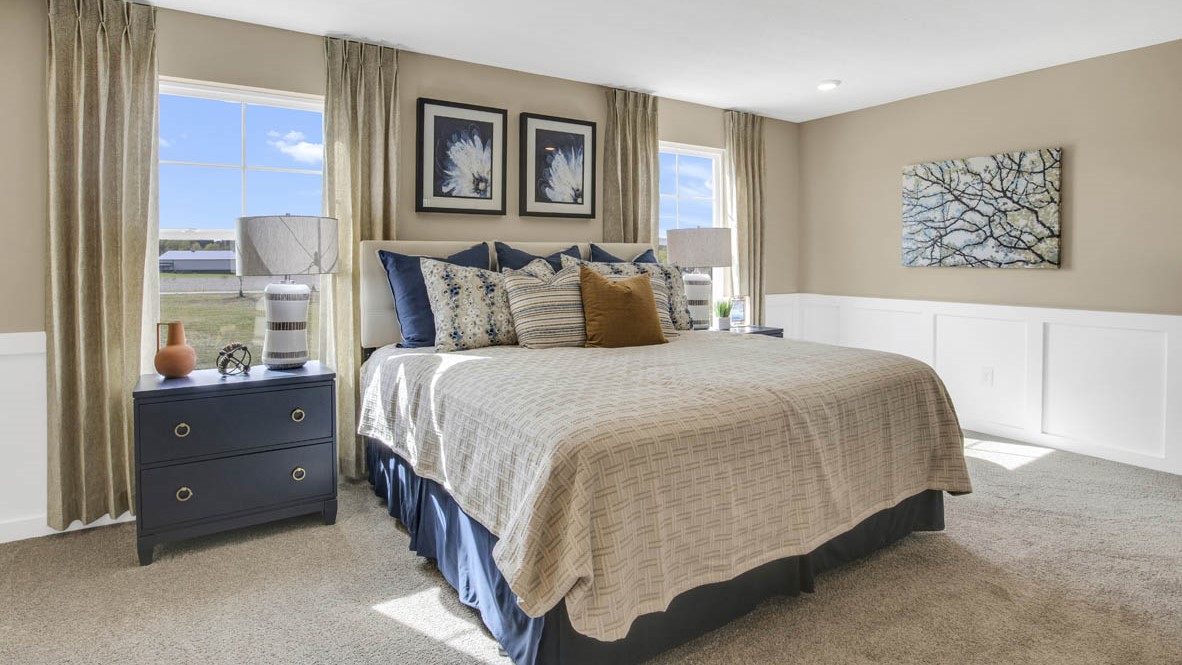 Primary bedroom with large bed, neutral and navy art, and carpet