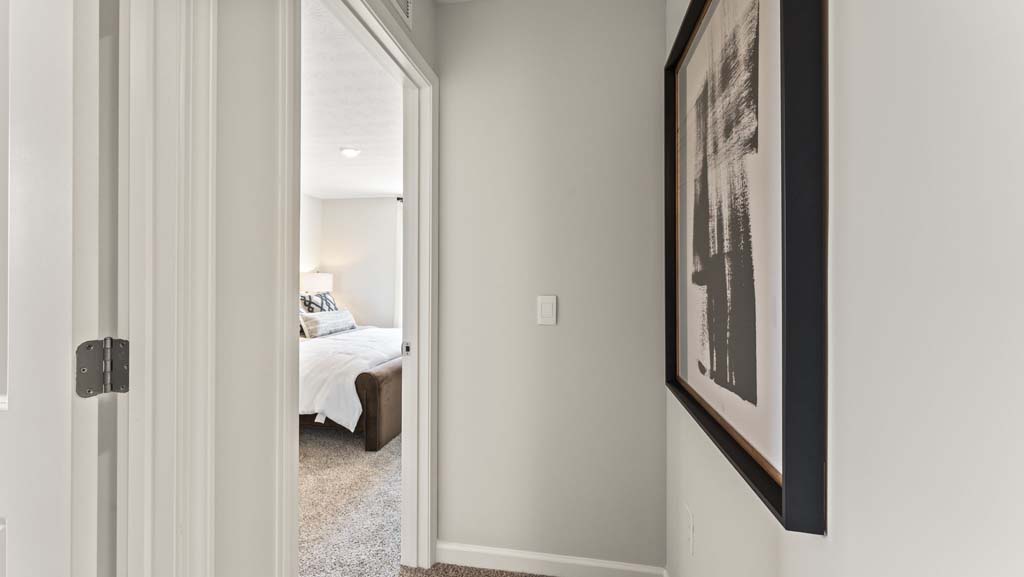 Hallway peering into bedroom with art on the wall and bed in door frame