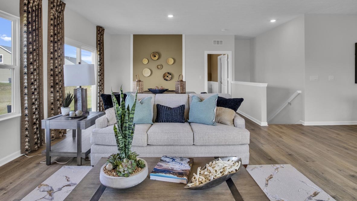 coffee table in living room with lush grey couch and dining room table, and door to primary bedroom.