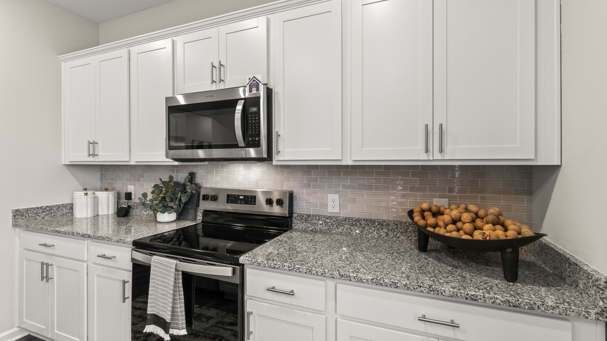 Closeup of granite countertop, oven range, microwave, and white cabinetry.