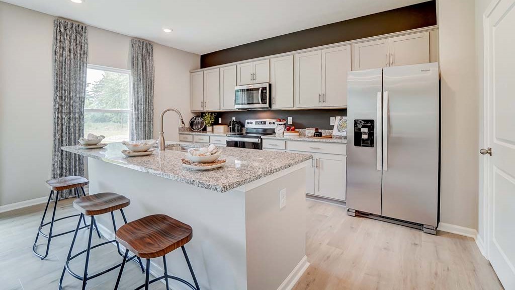 Full view of the open concept kitchen with gray cabinets and granite countertops with window and stainless steel appliances.