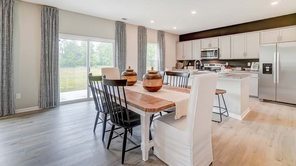 Dining room table and kitchen with windows.