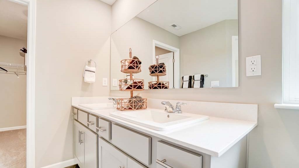 Primary bathroom with dual vanity sinks, large mirror, and view of the walk-in closet.