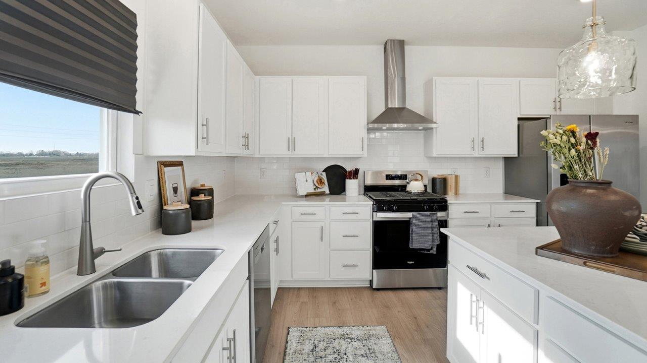 Bright white kitchen with a large island, black counter stools, stainless steel appliances, and three glass pendant lights.