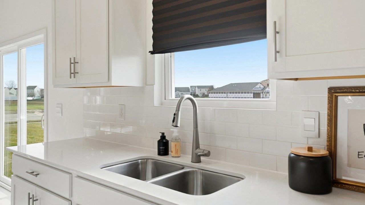 White kitchen with double-basin sink, stainless steel range and refrigerator, quartz counters, and island with floral decor.