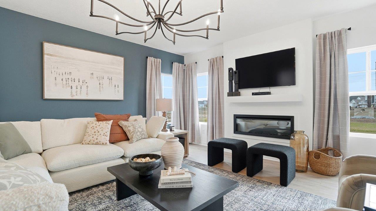 Open-concept living room with white sofas, two beige chairs, black coffee table, fireplace, dining area, and kitchen beyond.