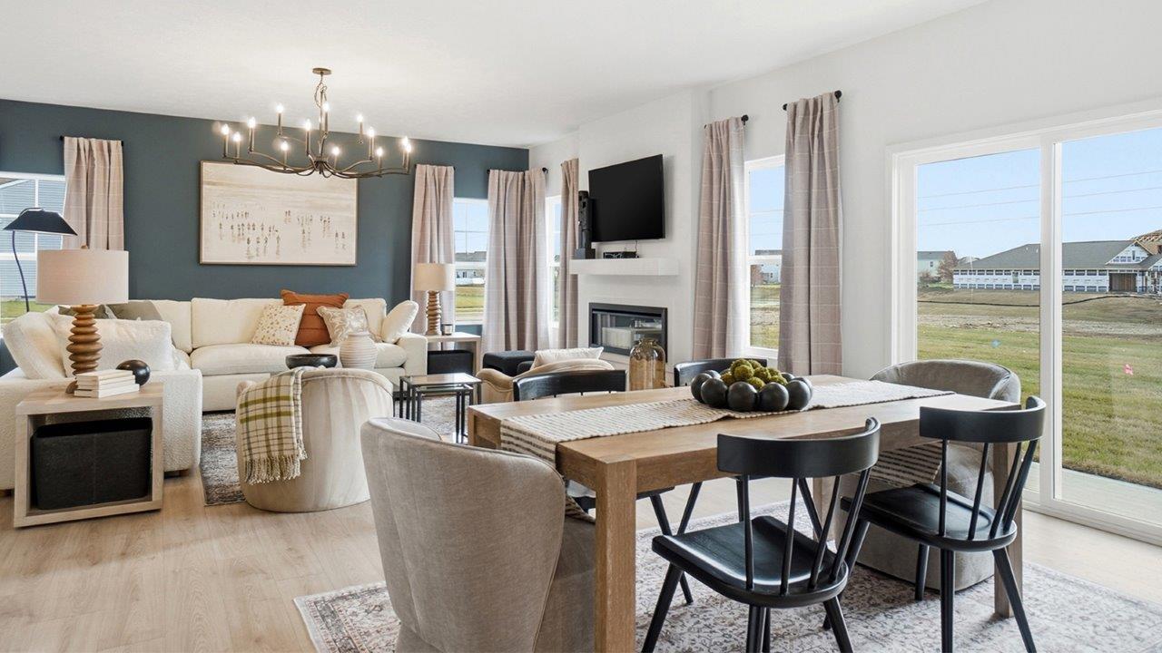 Open dining area with a rectangular wood table and mixed seating beside a white kitchen with island and pendant lights.