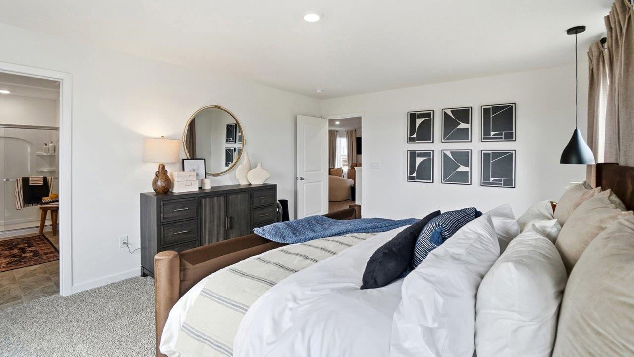 Primary bedroom with a brown upholstered bed, white bedding, blue throw, patterned nightstands, pendant lights, and black-and-white artwork.