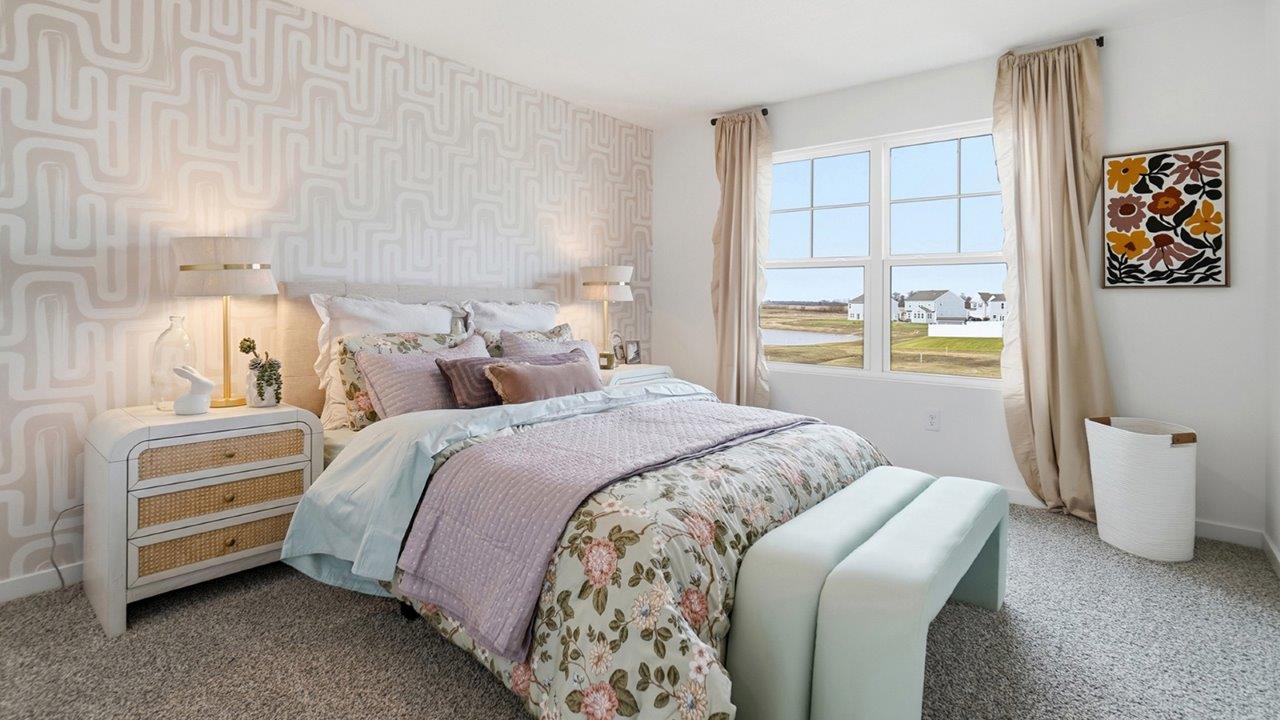 Bright bedroom with a floral-dressed bed, pale green bench, patterned accent wall, and sunlit window.