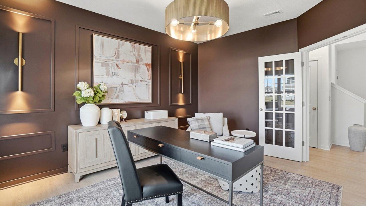 Home office viewed toward glass French doors, with a black desk, cream seating, artwork, and warm wall sconces.
