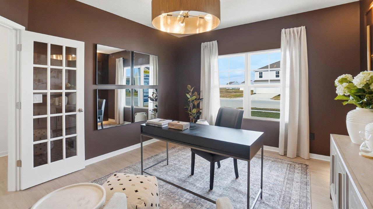 Home office with a black desk and chairs, dark brown walls, glass French door, built-in shelving, and sunny window.