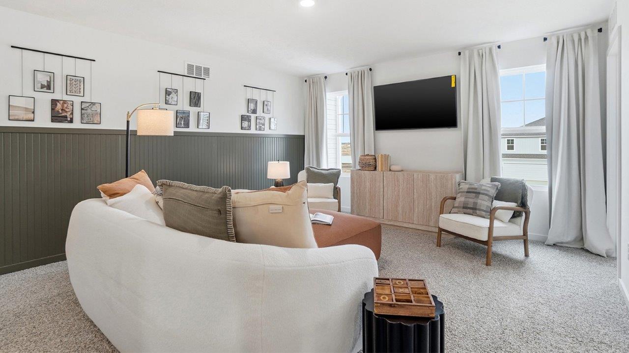 Upstairs loft with curved white sofa, wall-mounted television, two chairs, orange ottoman, and dark green wainscoting.