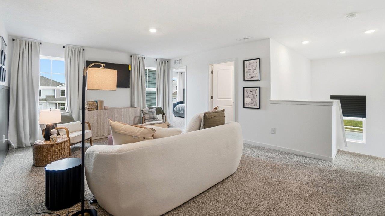 Wide upstairs loft with curved white sofa, television area, carpeted floor, hallway doors, and stair opening.