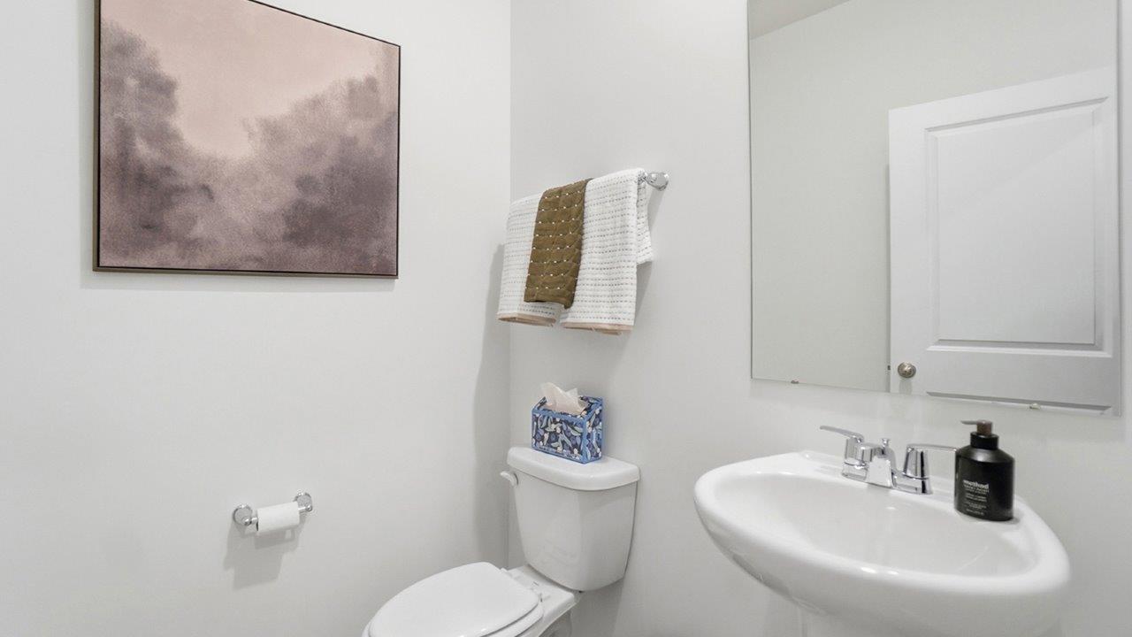 Compact powder room with a pedestal sink, rectangular mirror, toilet, towel rack, and abstract wall art.