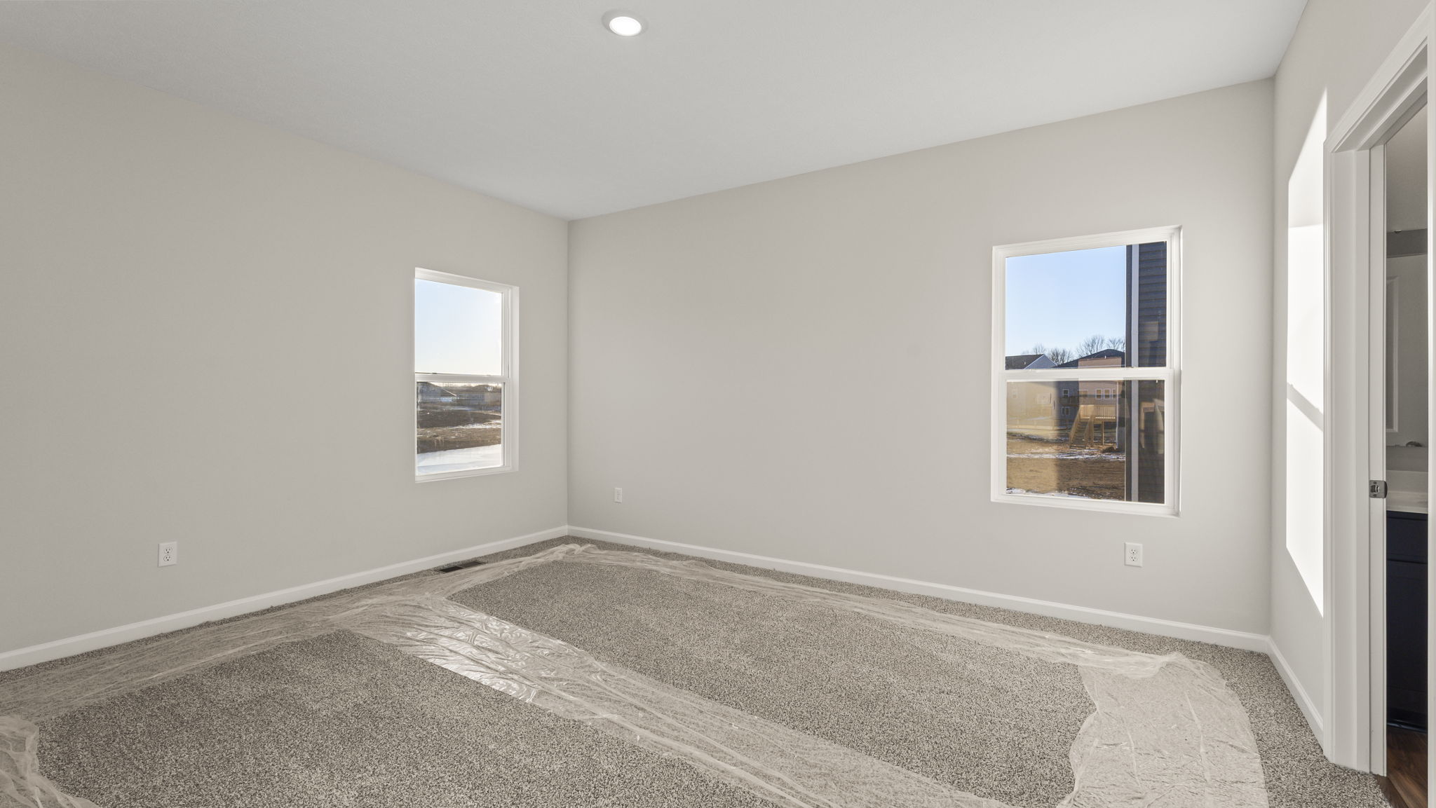 Primry bedroom with two windows, carpet, and door to primary bathroom