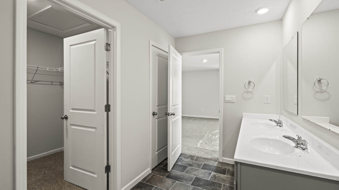 Primary bathroom looking into closet, primary bedroom, and double-sink vanity