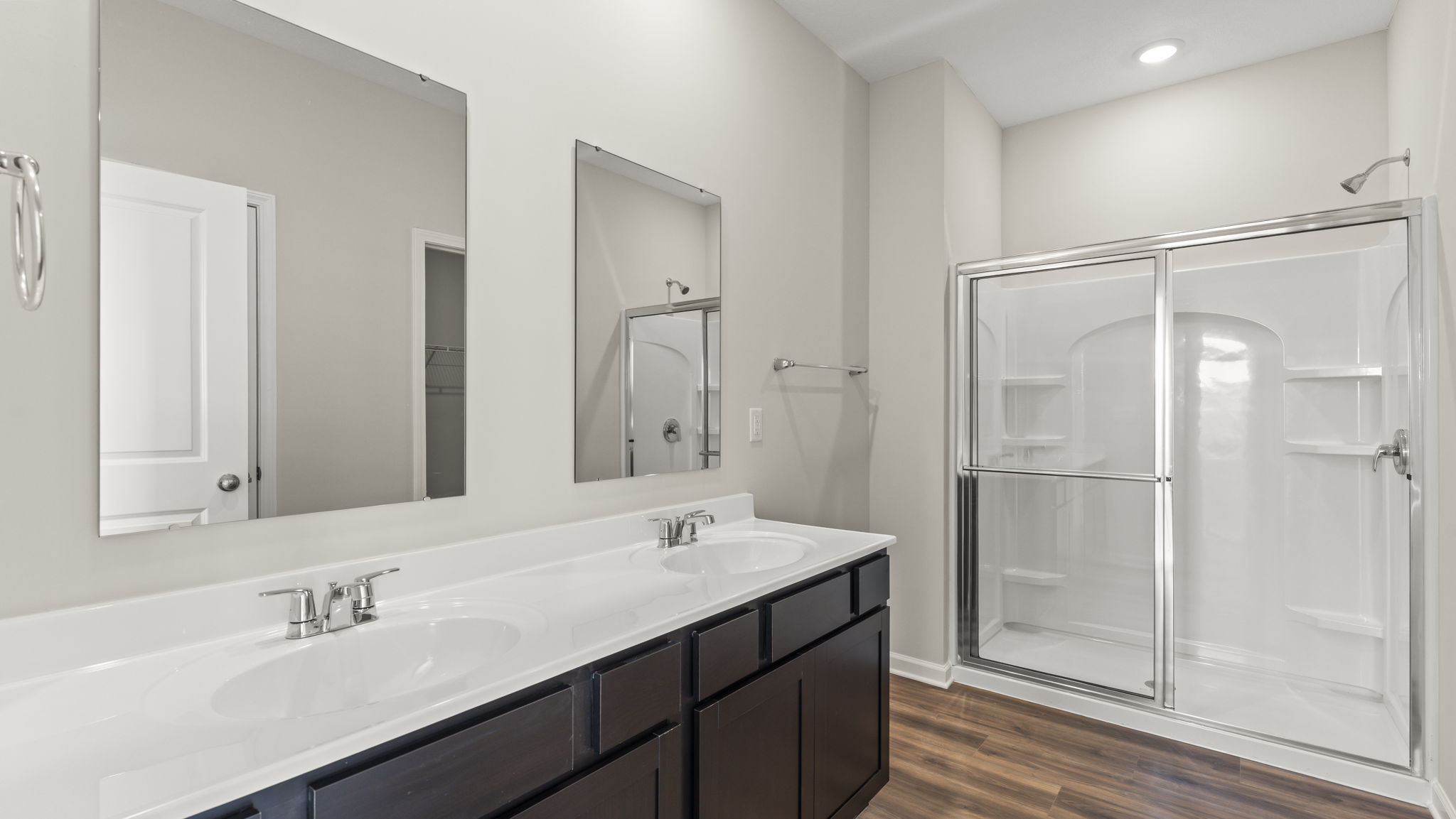 primary bathroom with dual-sink vanity, mirrors, and walk-in shower.