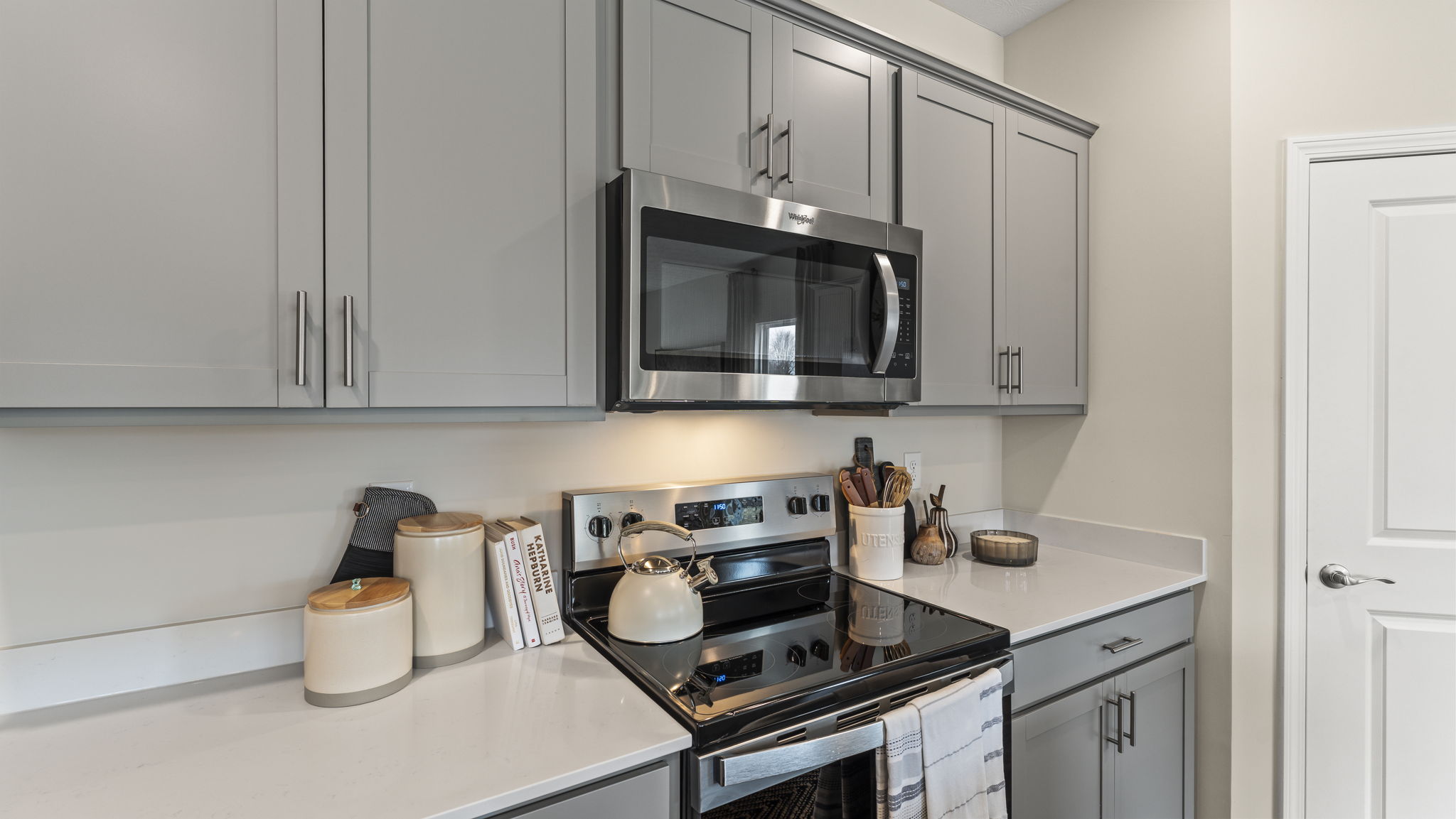 Oven range and wall-mounted microwave between quartz countertops and gray cabinetry respectively.