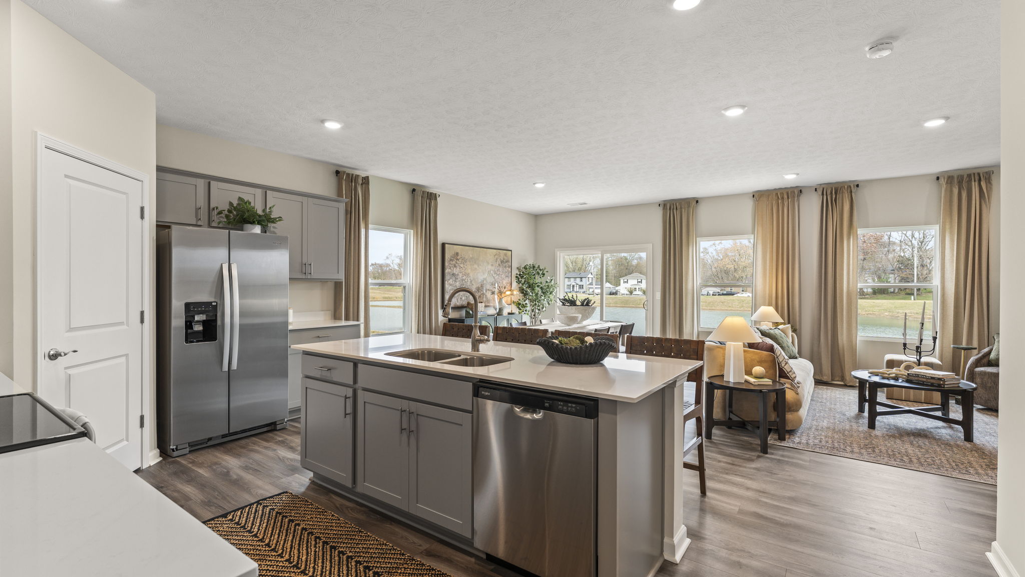 View from the kitchen into the living room with stainless steel appliances, quartz island, and earthy decoration.