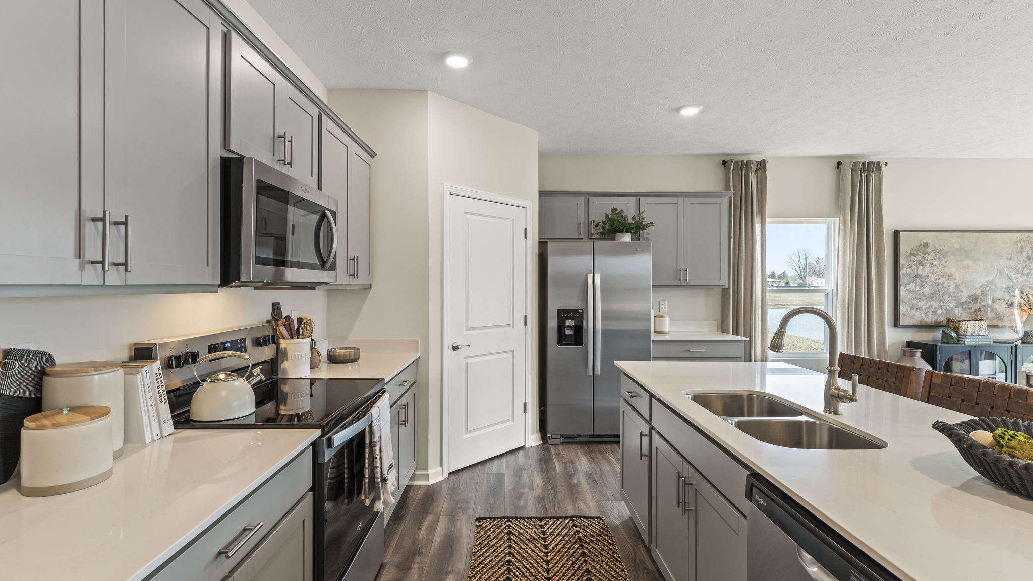 Side view of kitchen with quartz countertops, stainless steel appliances, door to pantry, and island on the right of frame.