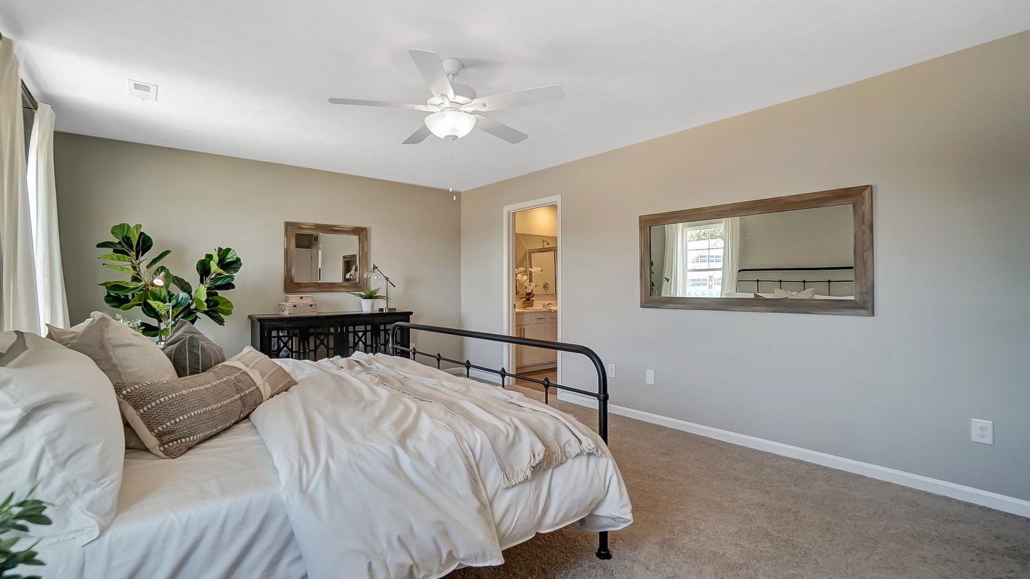 Window view of Primary bedroom with bed and elegant mirrors with view of private bathroom.