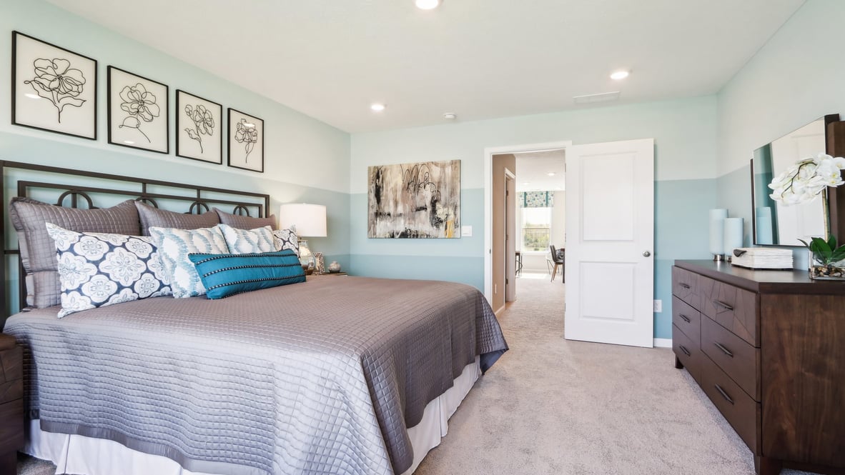 Three-quarter view of primary bedroom with art on walls and primary bathroom in the back.