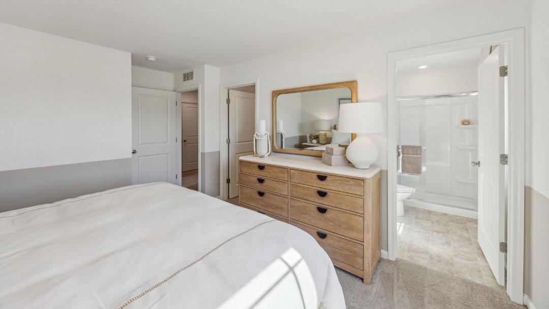 spacious bedroom with white and beige colored decor, featuring a wooden nighstand on each side of the bed, a large window, and a wooden dresser