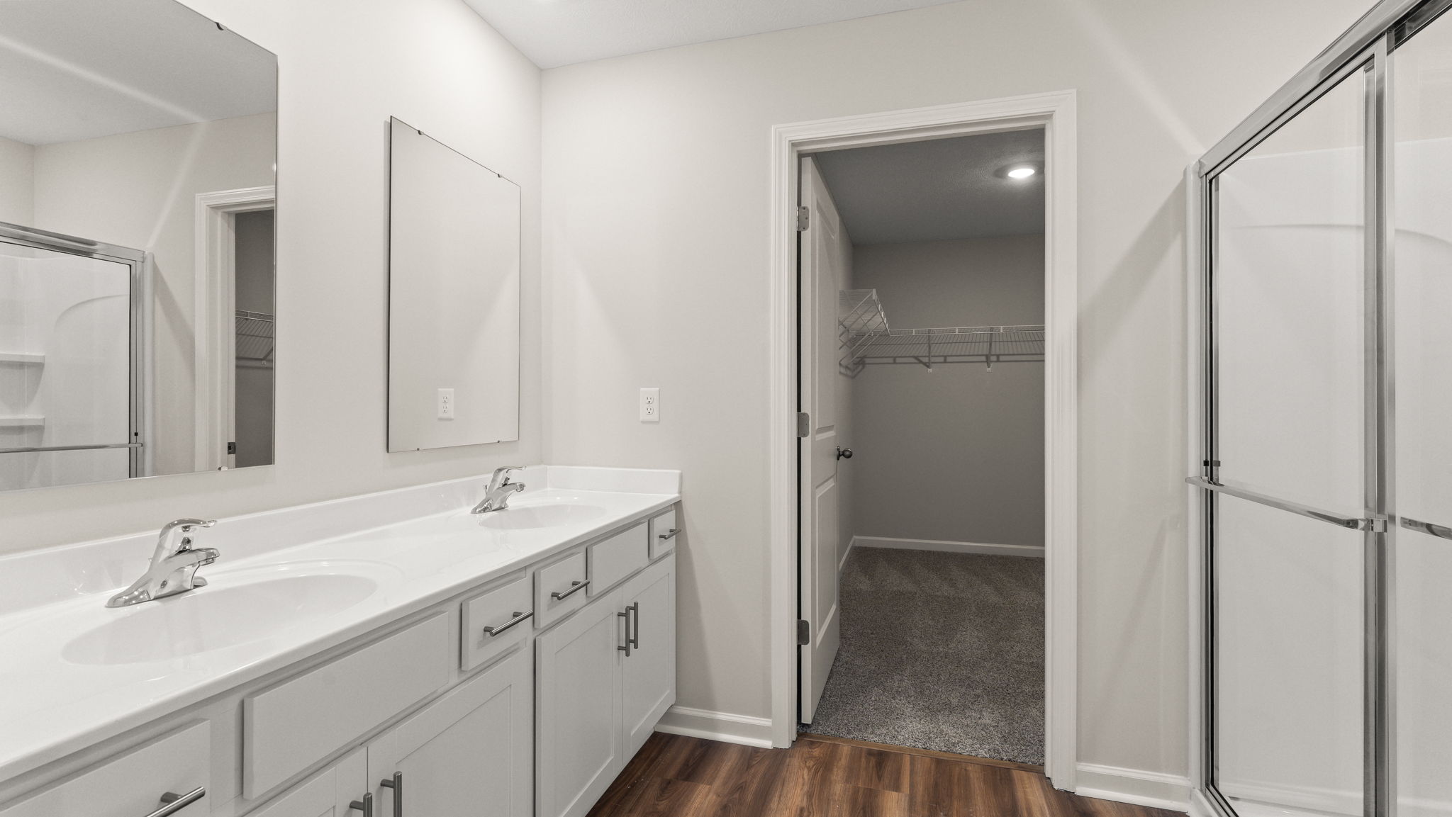 Primary bathroom with dual-sink vanities, walk-in closet, and walk-in shower