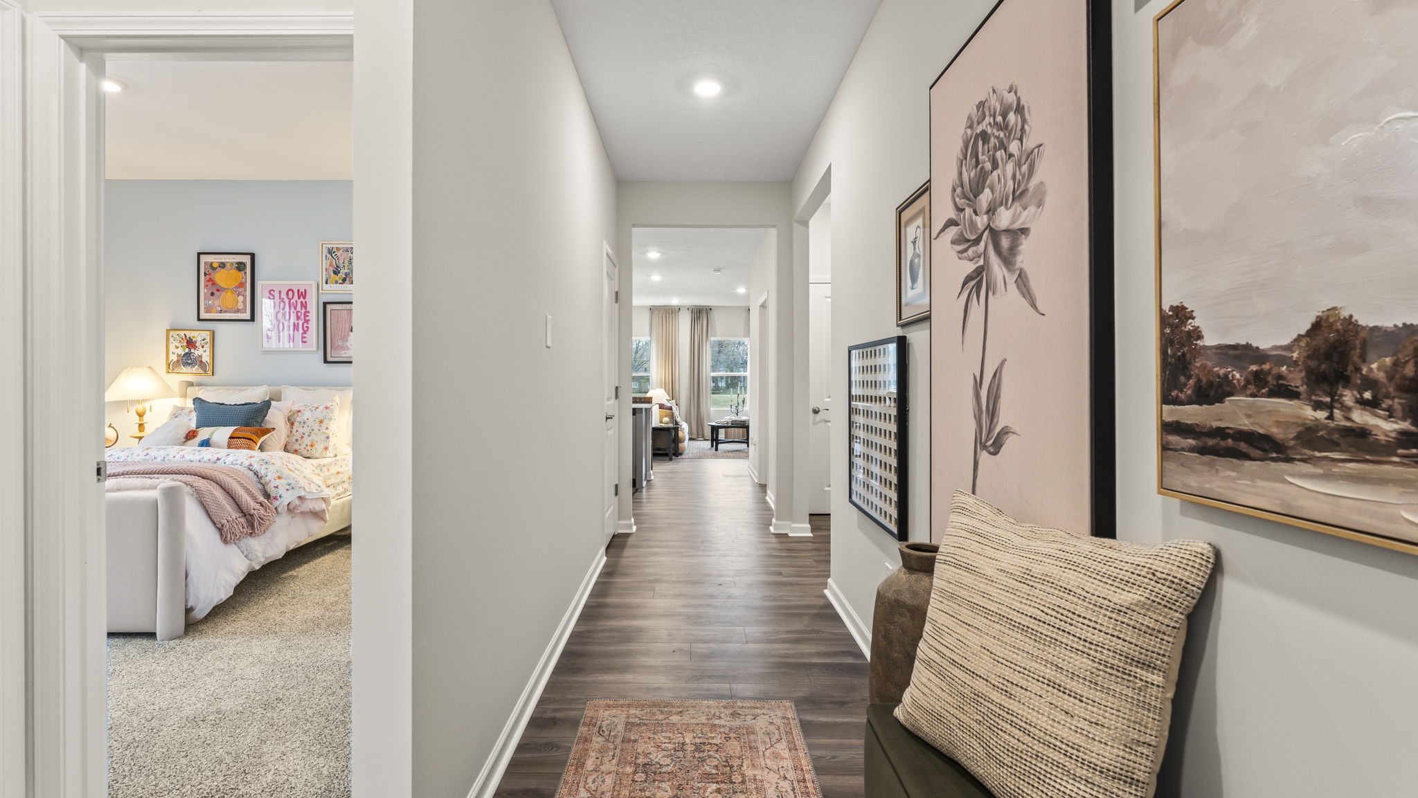 Hallway at the front of the home with view of bedroom on the left, living room in the center, and large print art on the right of nature and pottery.