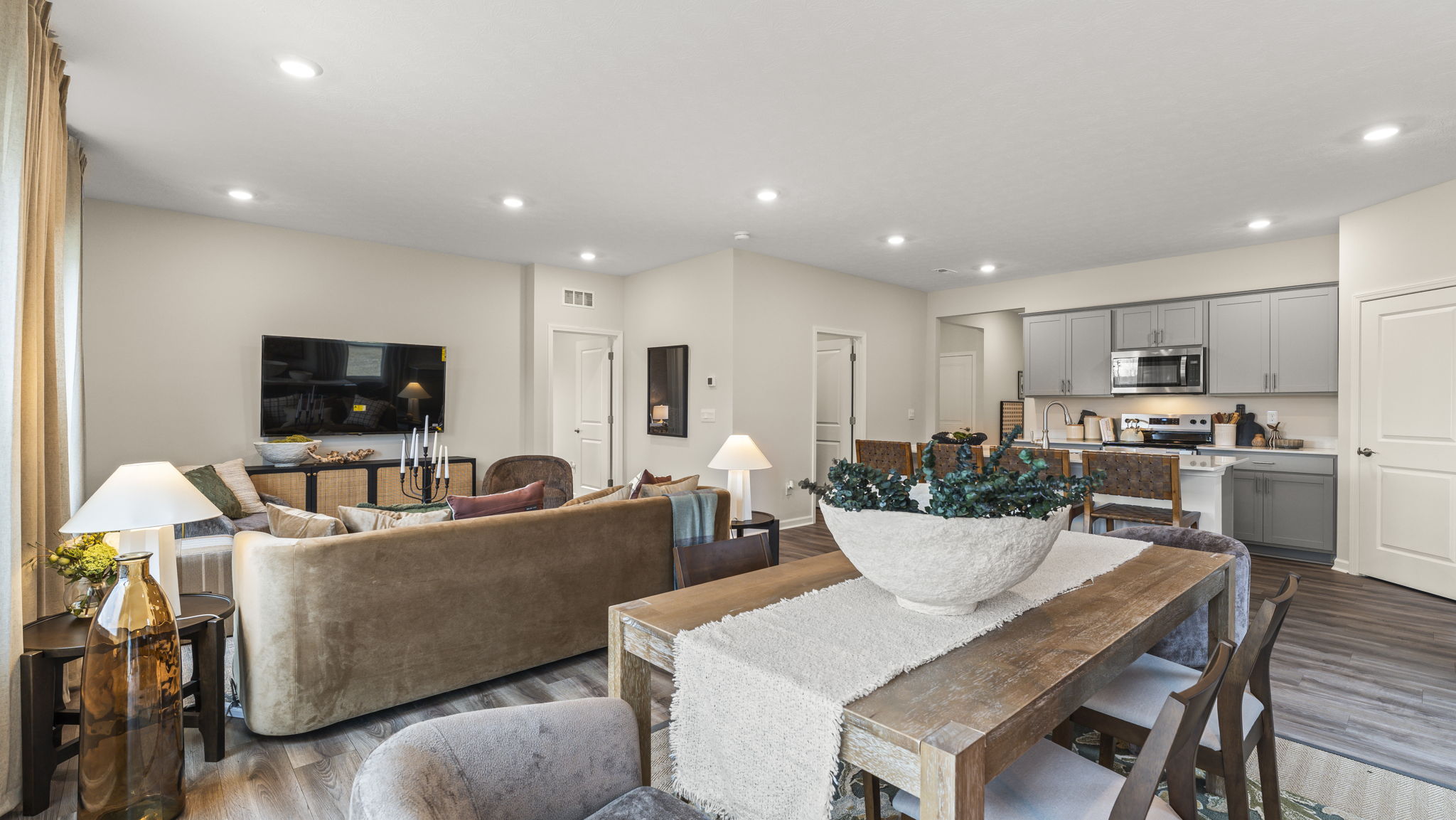 Full kitchen, dining, and living areas with earthy tones, brown and white furniture, and doors to auxillary rooms.