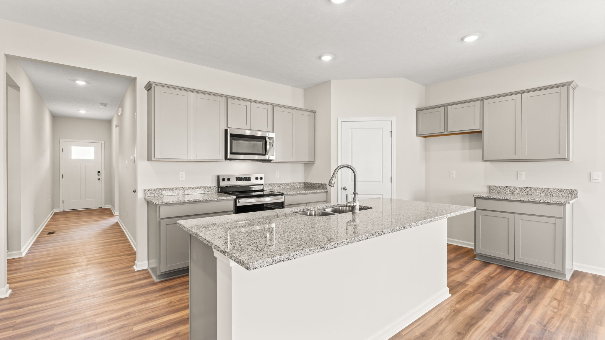 Wide image of a kitchen with gray cabinets, large granite countertops, and appliances