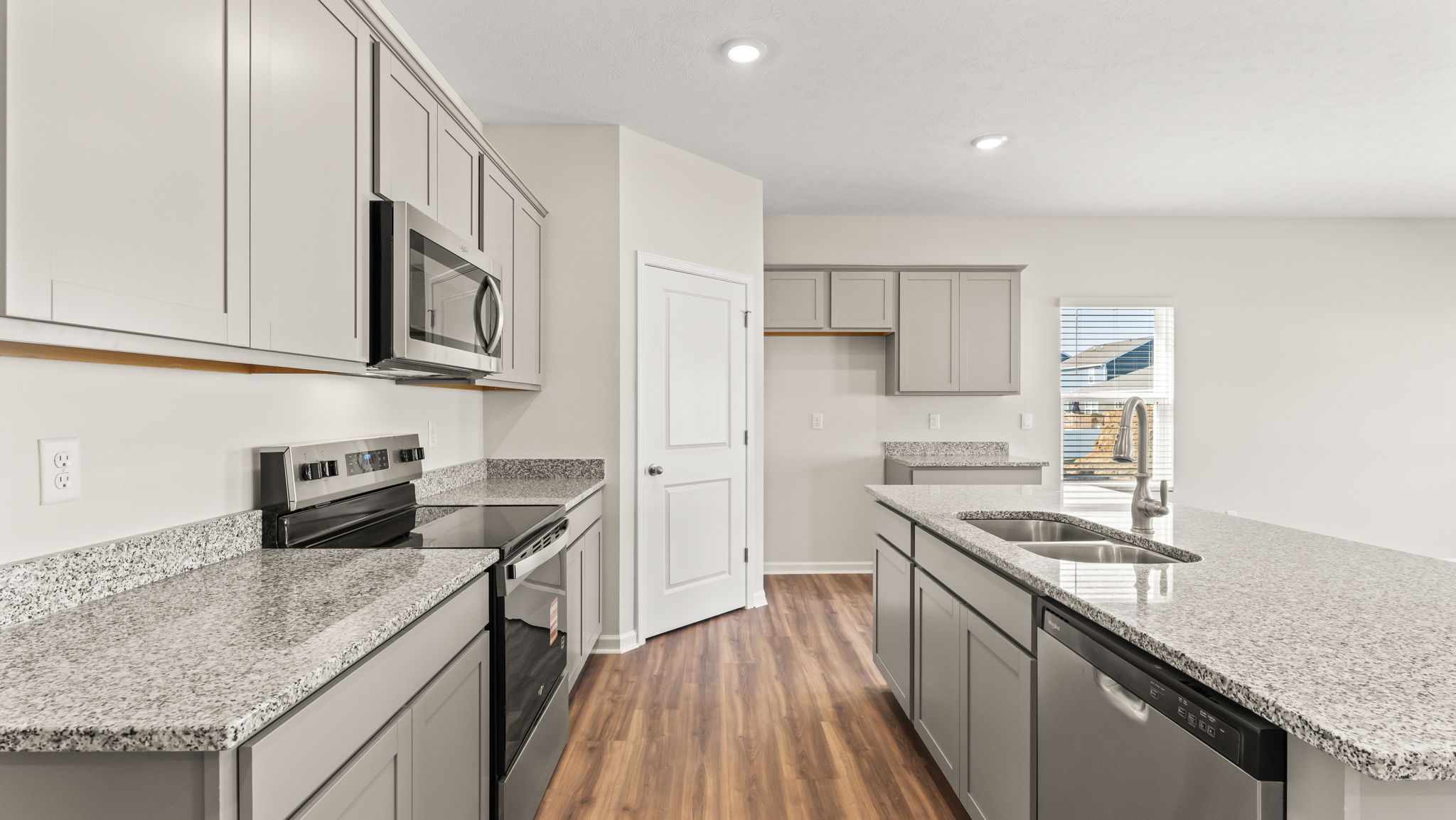 Side view of kitchen with countertops and microwave on the left, pantry in the center, and granite island on the right.