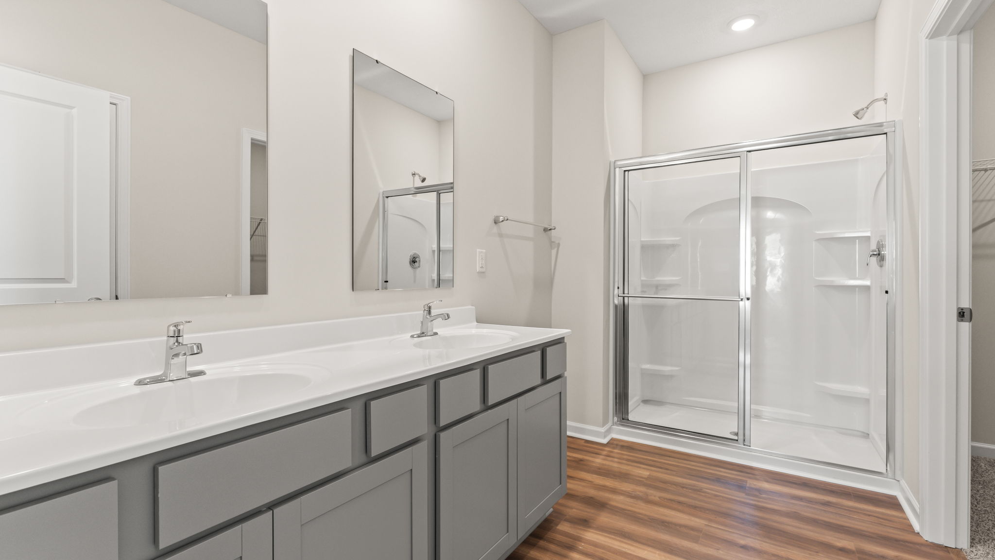 Primary bathroom with dual-mirror and double bowl vanity. A shower with a glass door is in the rear.