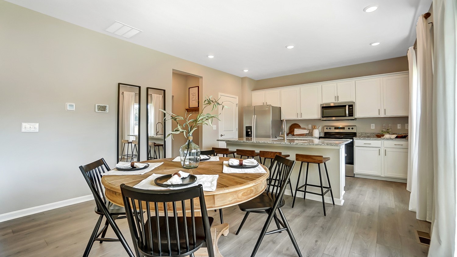 Modern Open Concept view of the great room with wood table white cabinets and stainless steel appliances and natural lighting.