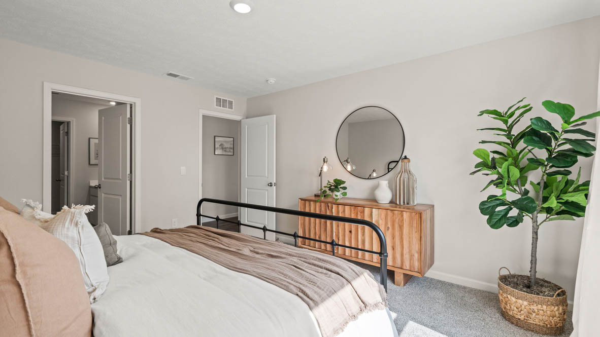 Primary bedroom with wood dresser, plants, circular mirror.